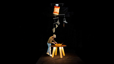 Szene mit Person an einem Tisch im dunklen Raum mit orangefarbenem Spotlight.